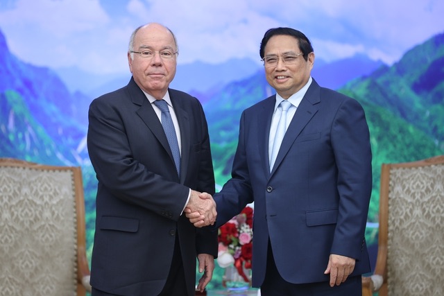 Mauro Vieira shaking hands with a host in front of a painted mountain landscape