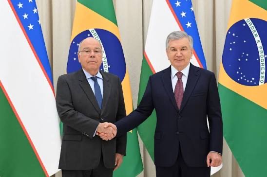 Mauro Vieira shaking hands with a host between the flags of Uzbekistan and Brazil