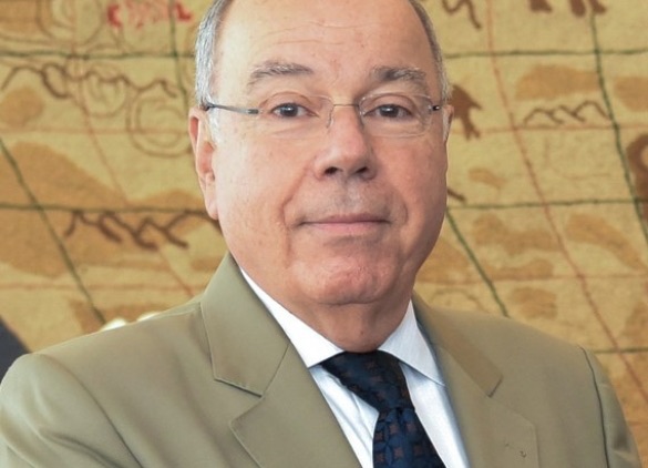 Portrait of Mauro Vieira in a light suit and dark tie, in front of an antique map tapestry