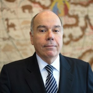 Portrait of Mauro Vieira in a dark suit and striped tie before an antique map