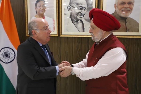 Mauro Vieira clasping hands with an Indian official wearing a red turban, Indian flag and framed portraits behind