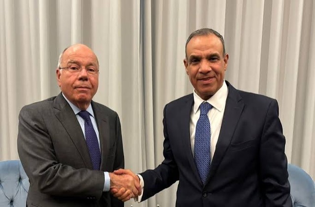 Mauro Vieira shaking hands with a counterpart in a room with cream curtains
