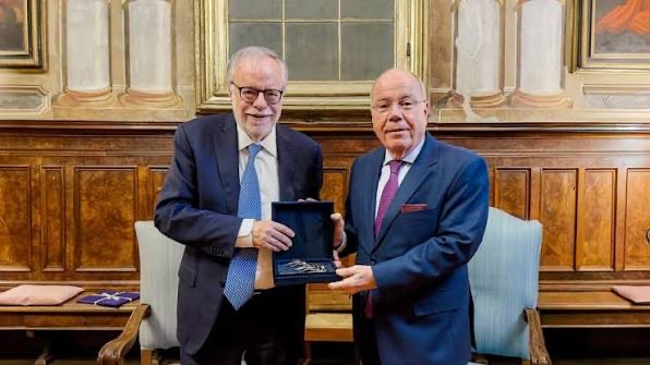 Mauro Vieira and another man standing in a wood-panelled historic hall, one holding an open presentation box