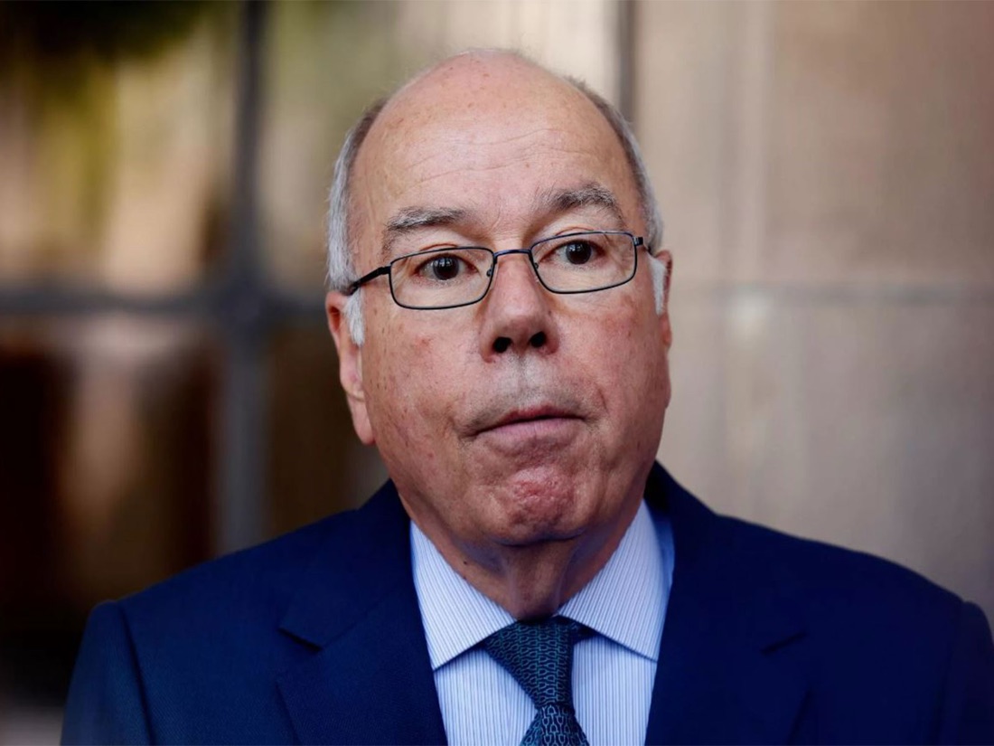 Close-up portrait of Mauro Vieira in glasses, dark suit and blue patterned tie, against a softly blurred background