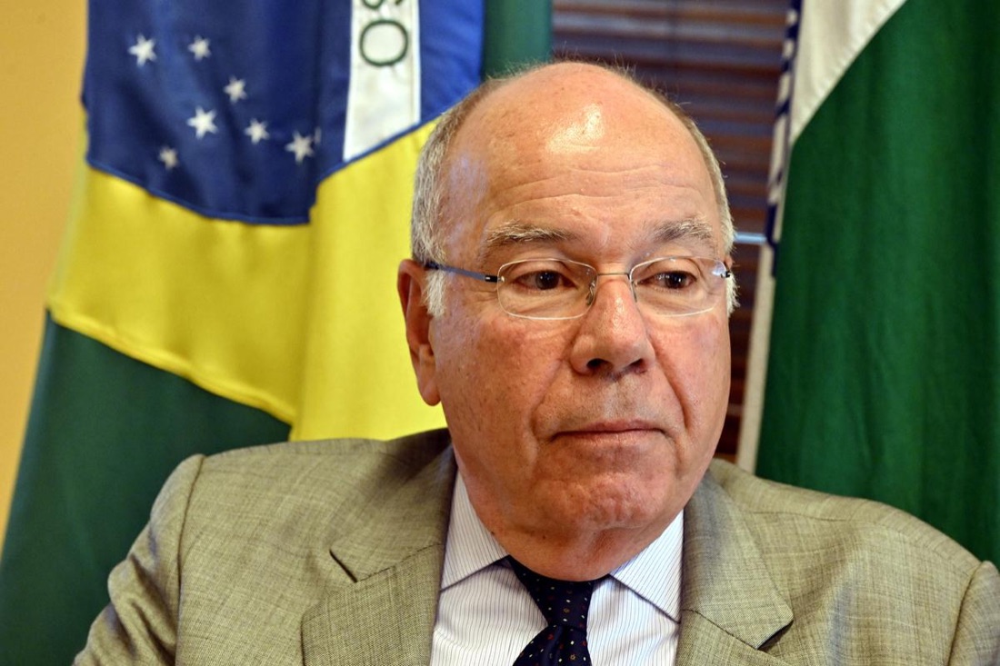 Close portrait of Mauro Vieira in rimless glasses and a light suit, Brazilian and Indian flags behind him
