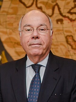 Official-style portrait of Mauro Vieira in a dark suit and patterned tie before a historic map